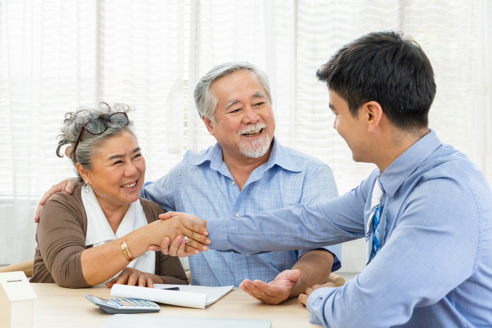Couple smiling and shaking hands with a professional during a meeting.
